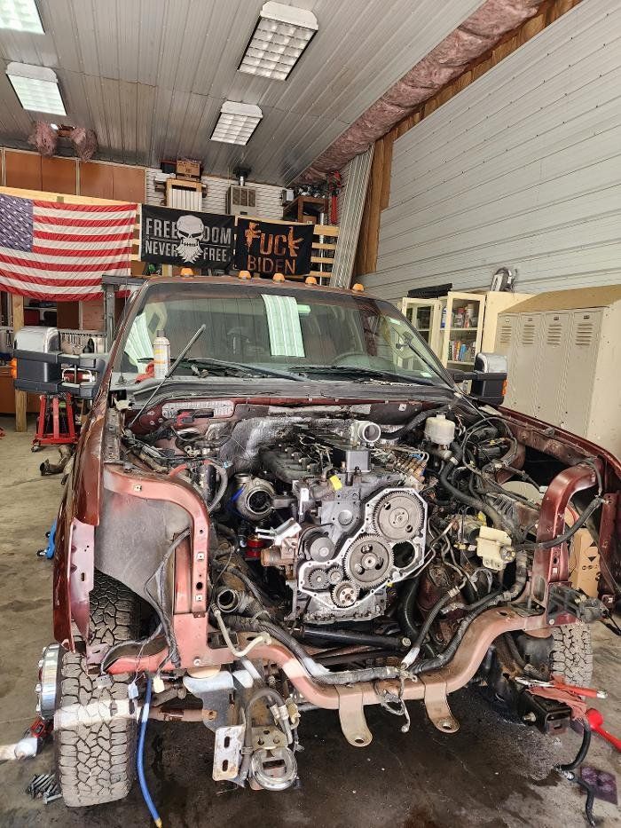 Red pickup truck under repair in a garage; engine exposed. American flag and shop signage visible.