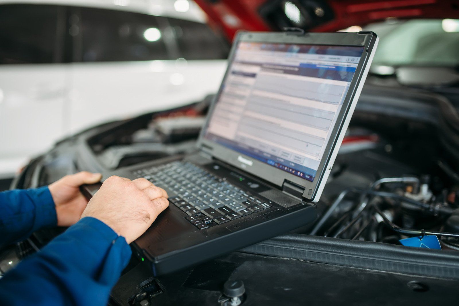 Mechanic using a laptop for car diagnostics in an auto shop.