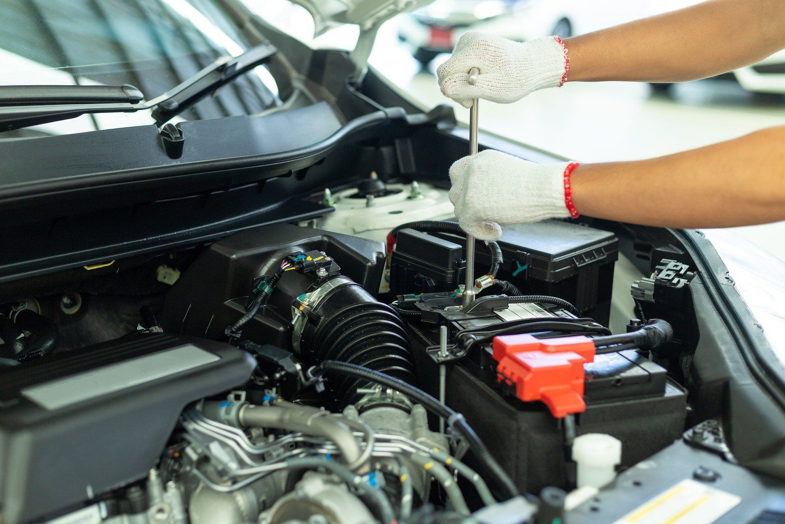Mechanic in gloves using a wrench to work on a car engine in a repair shop.
