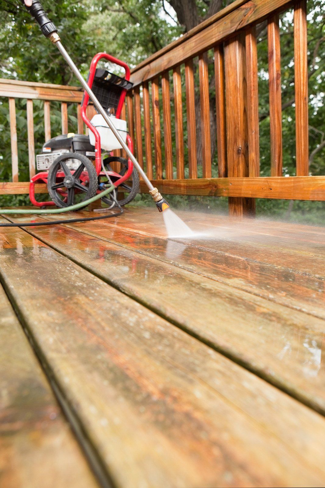 A person power washing a wooden deck with a pressure washer; water spraying.