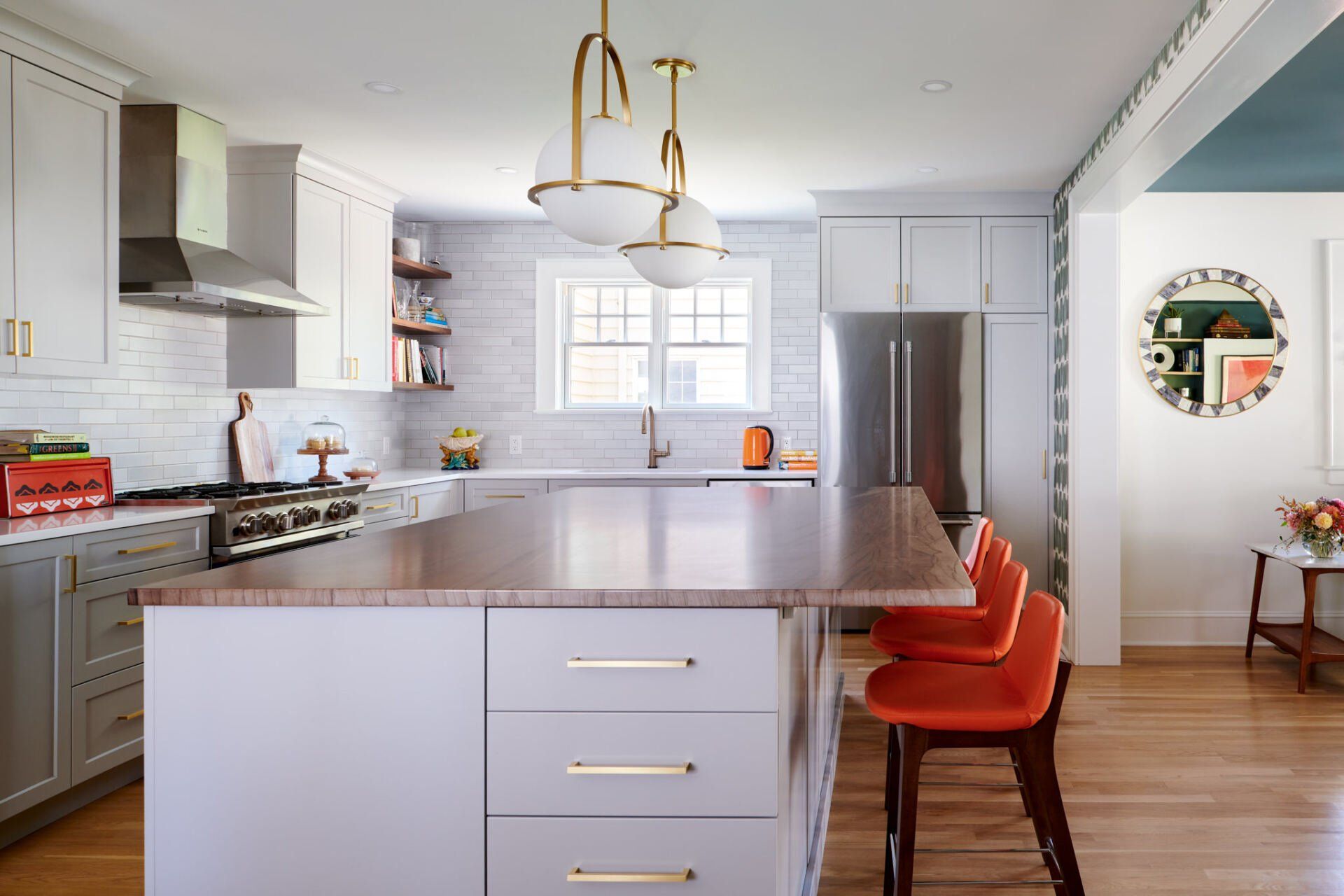 A kitchen with white cabinets , stainless steel appliances , a large island , and orange chairs.