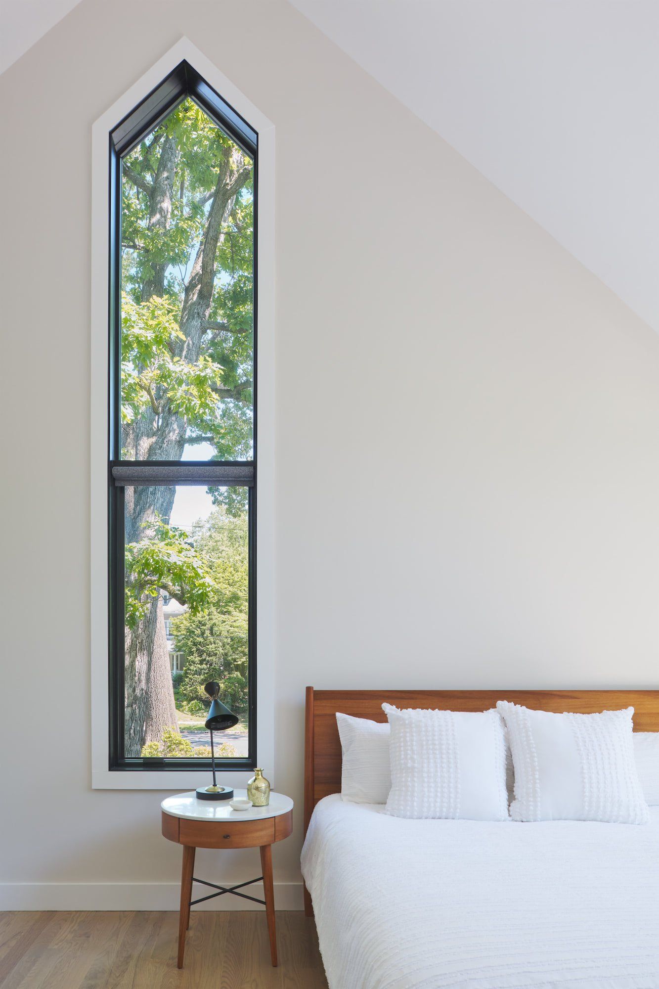 A bedroom with a bed , nightstand , and large window.