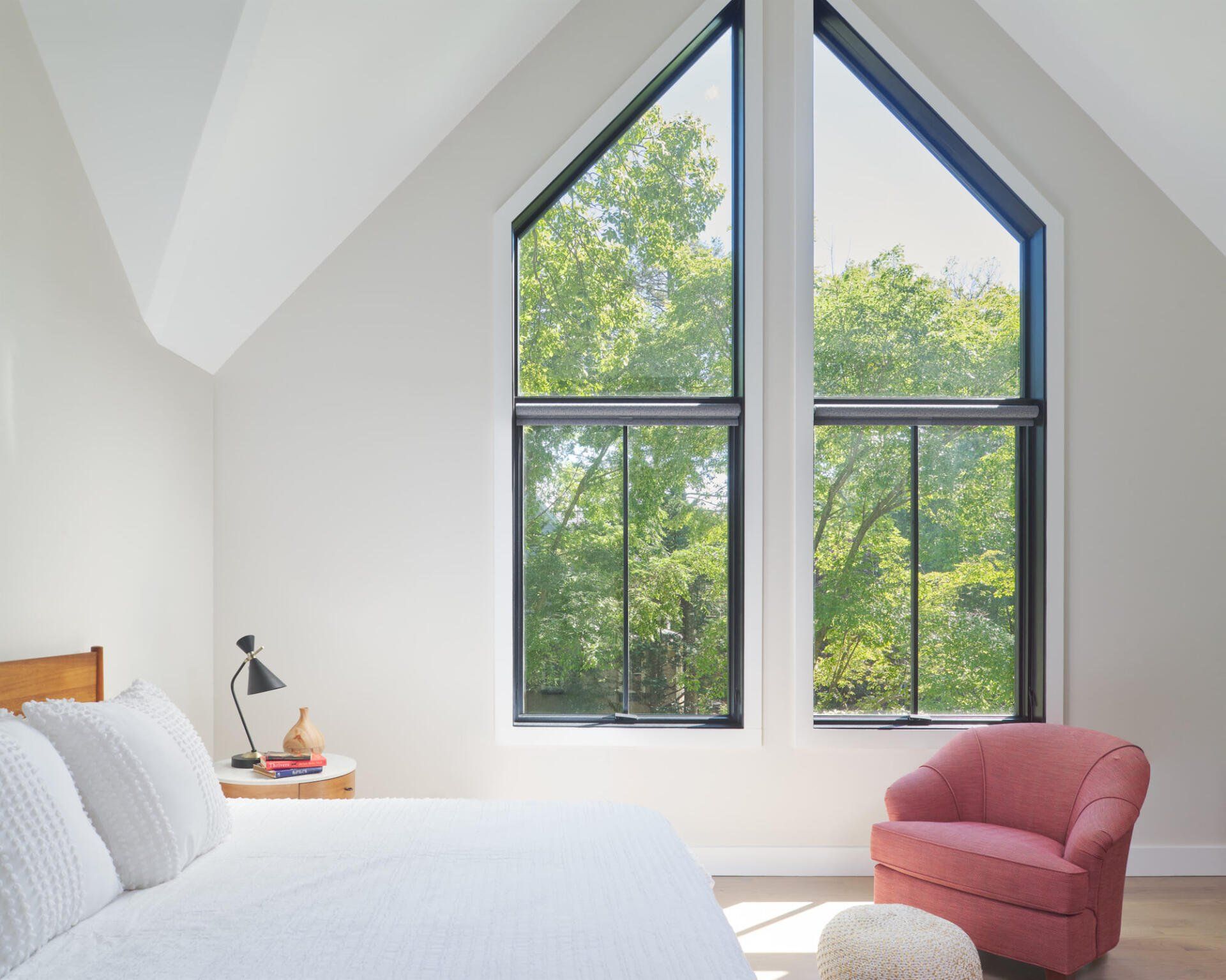 A bedroom with a bed , chair , and two large windows.