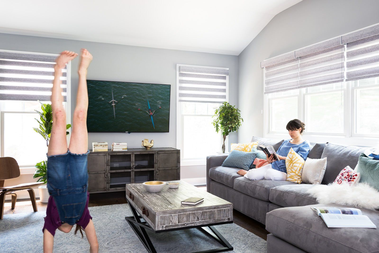 A girl is doing a handstand in a living room while a man sits on a couch.