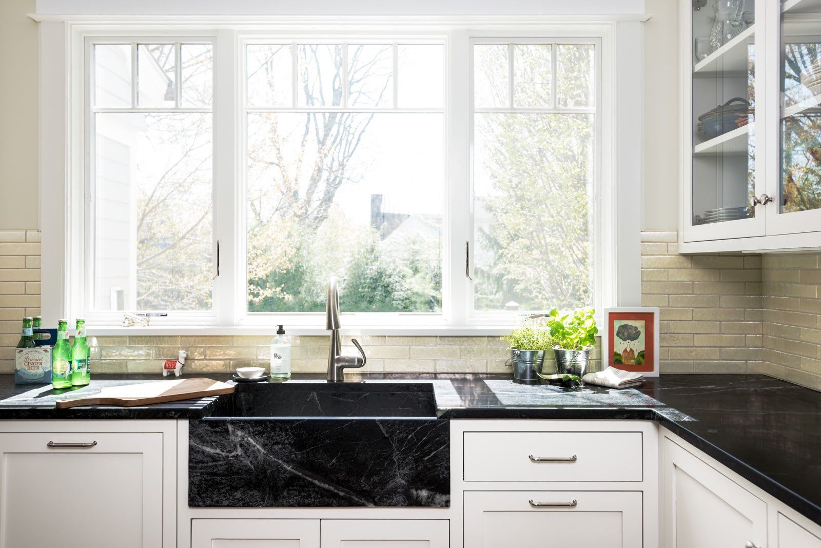 A kitchen with a black sink , white cabinets , and a window.