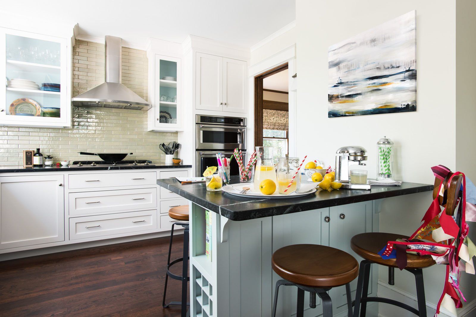 A kitchen with a large island and stools and a painting on the wall.