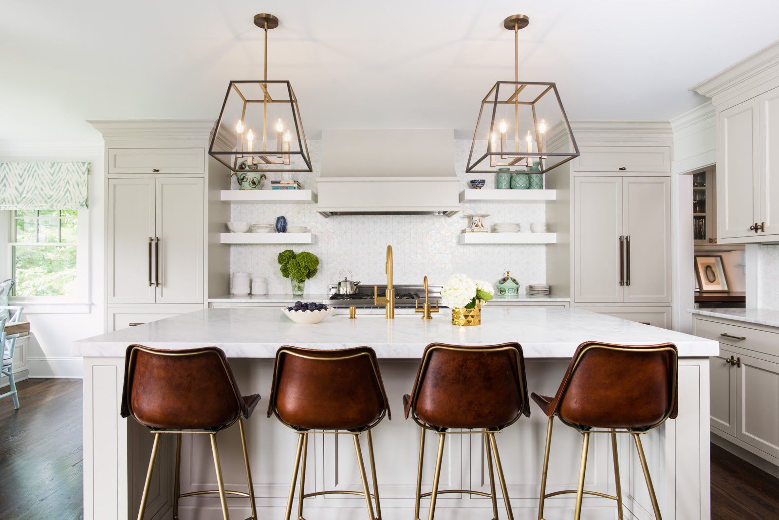 A kitchen with white cabinets and brown leather bar stools.