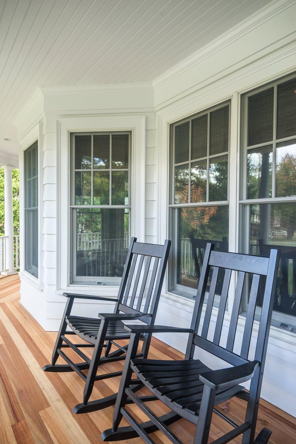 Two black rocking chairs are sitting on a porch next to a window.