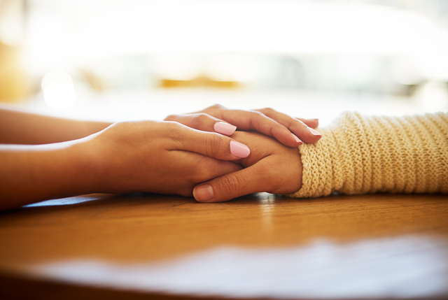 Two women are holding hands on a wooden table.