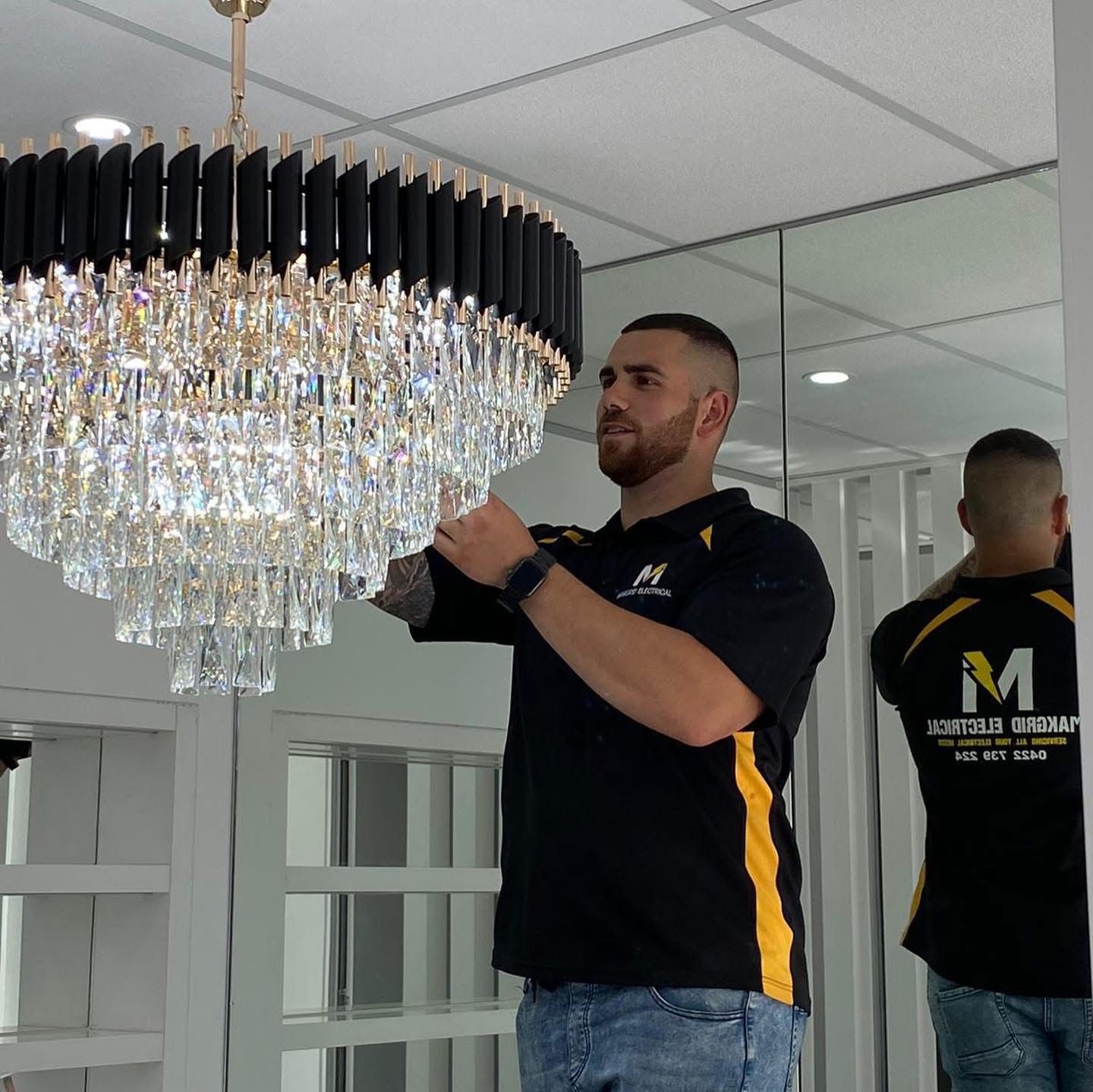 A man in a black shirt with the letter m on the back is working on a chandelier