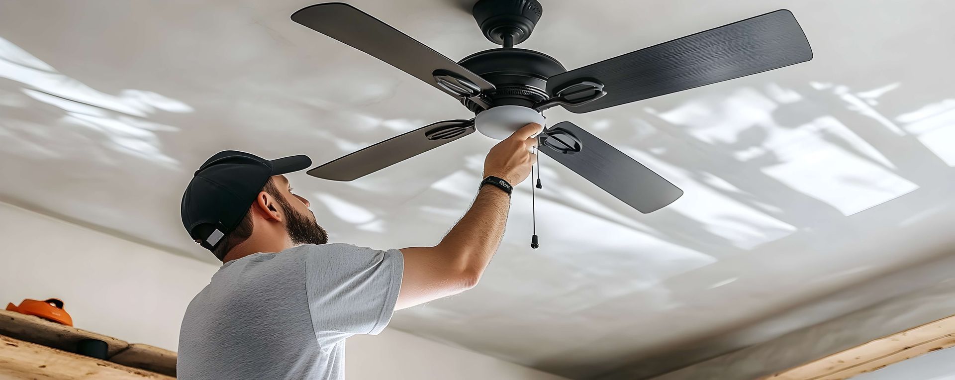 A man is installing a ceiling fan in a room.