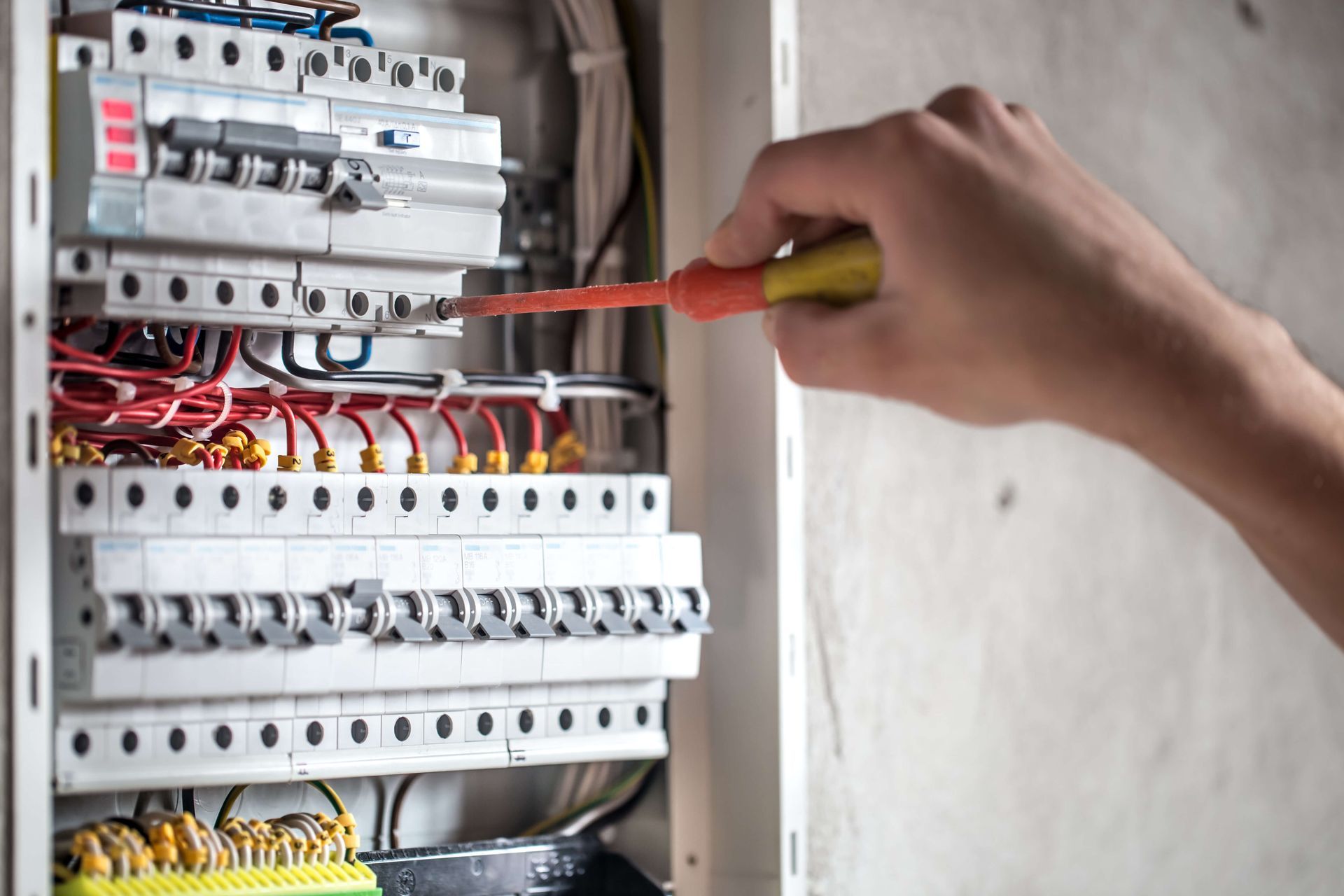 A person is working on an electrical box with a screwdriver.