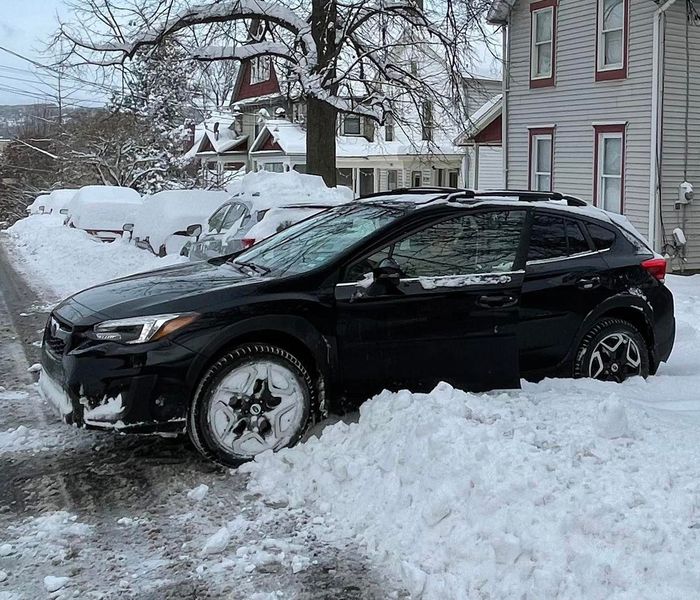 Black Subaru SUV stuck in deep snow on a street in front of houses during winter.