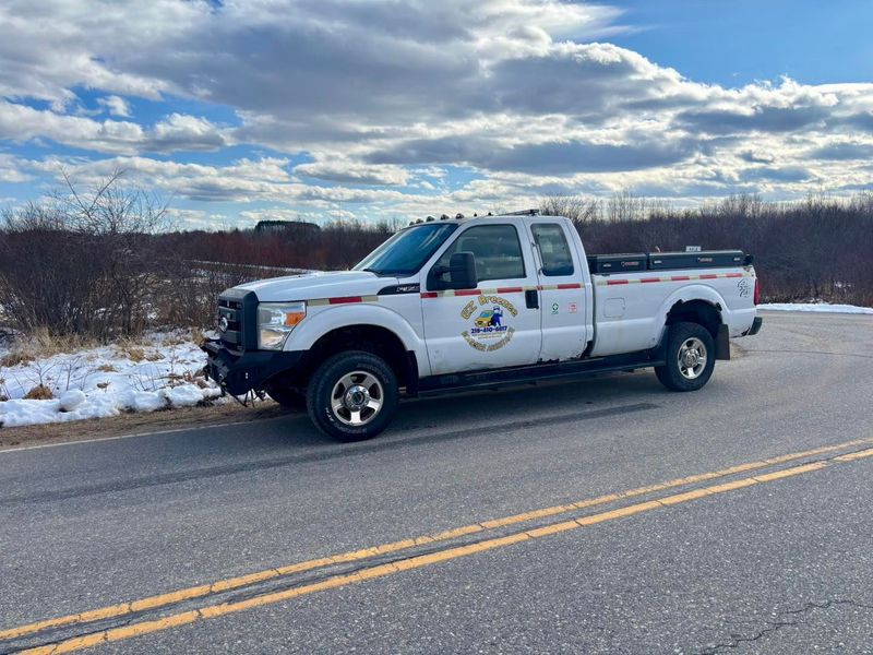 White work truck parked on a road with snowy roadside in a field under a cloudy sky.