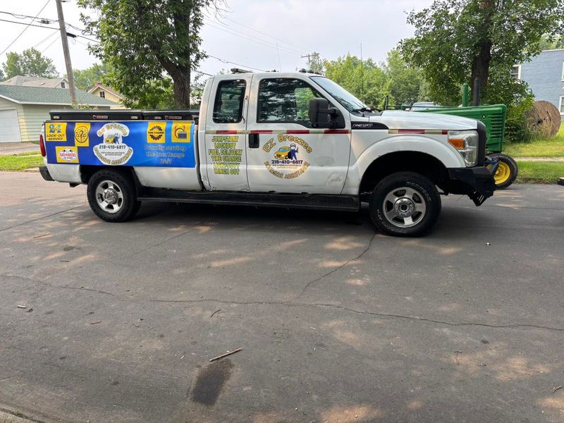 White pickup truck with business logos parked on a street; a John Deere tractor is in the background.