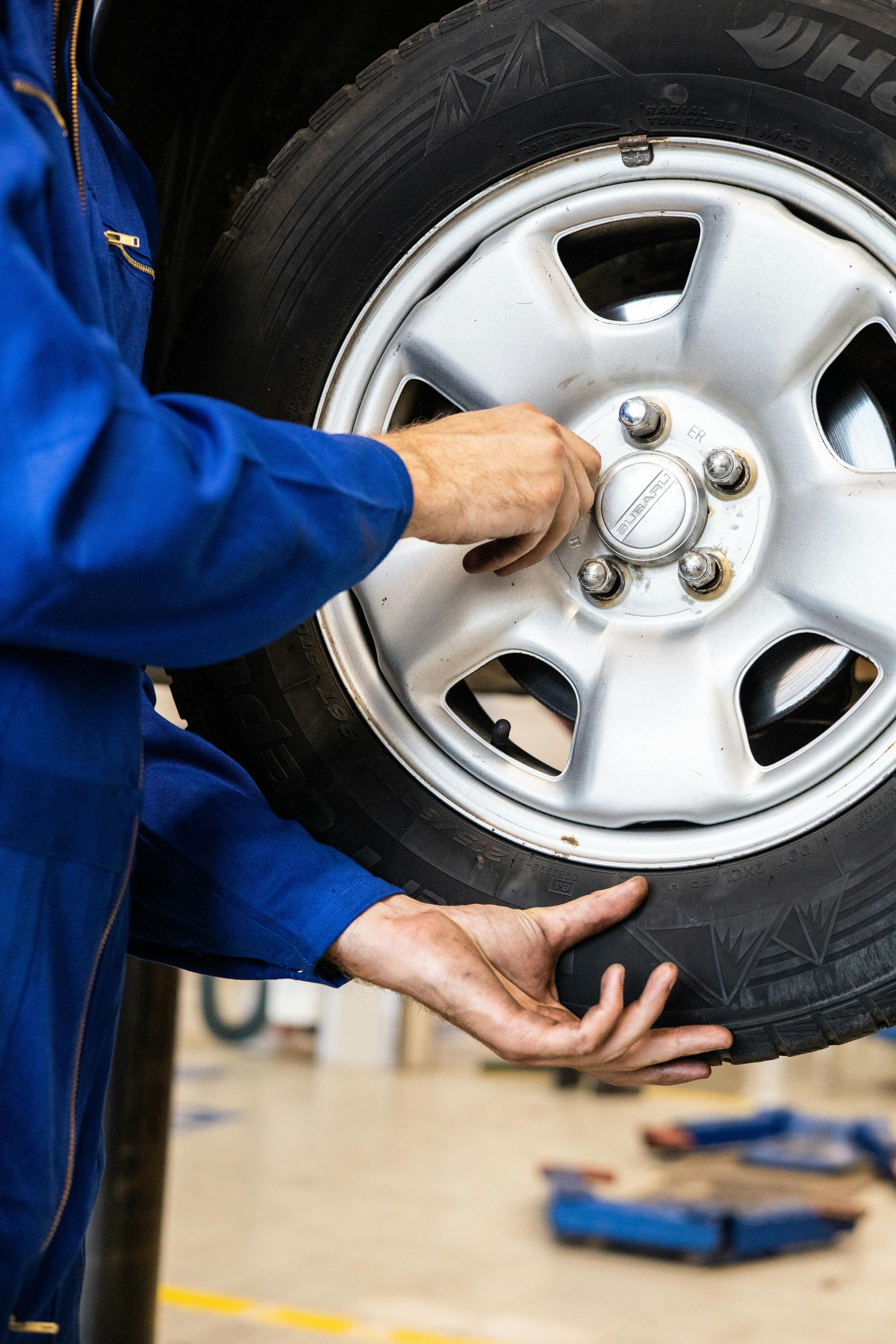 Person in blue coveralls removing lug nuts from a car tire.