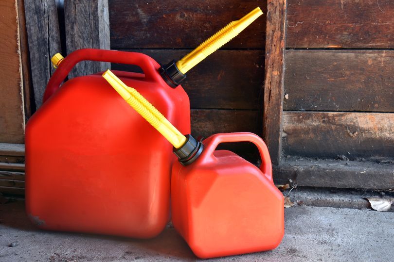 Two red gas cans with yellow spouts. Leaning against a wooden wall.