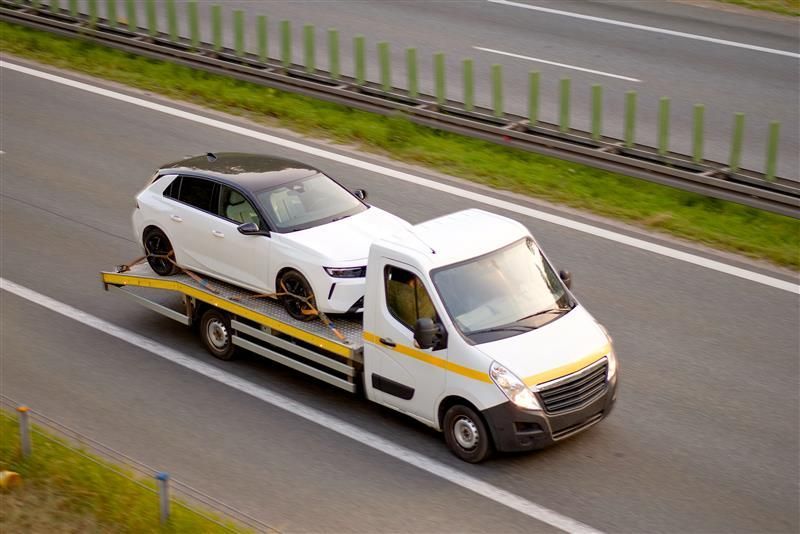 White car being towed on a flatbed truck on a highway.