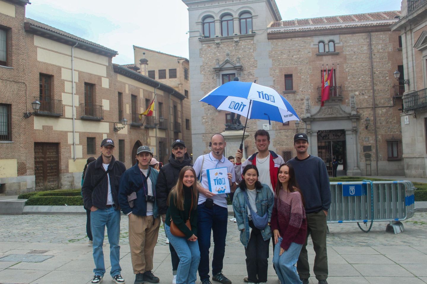 A friendly Tío Tours guide with a blue umbrella leads a group in a historic Madrid square during a Madrid Free Walking Tour.