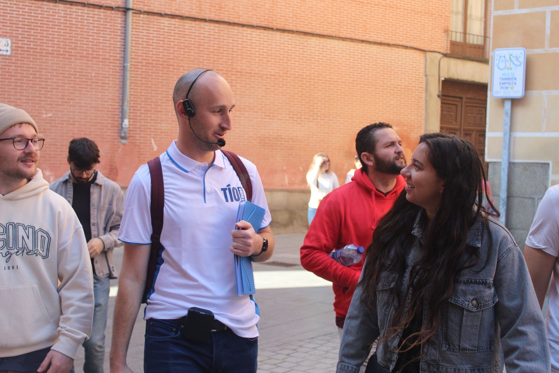 Tío tour guide leads a Madrid Free Walking Tour, engaging with smiling guests on a sunny street lined with brick buildings.