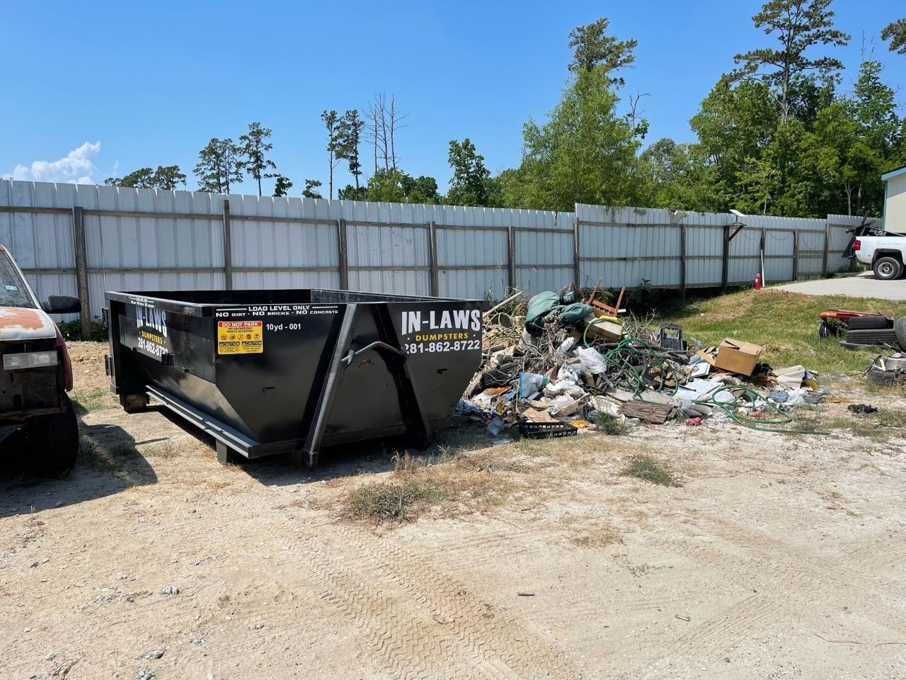 A dumpster is sitting next to a pile of trash in a dirt field.