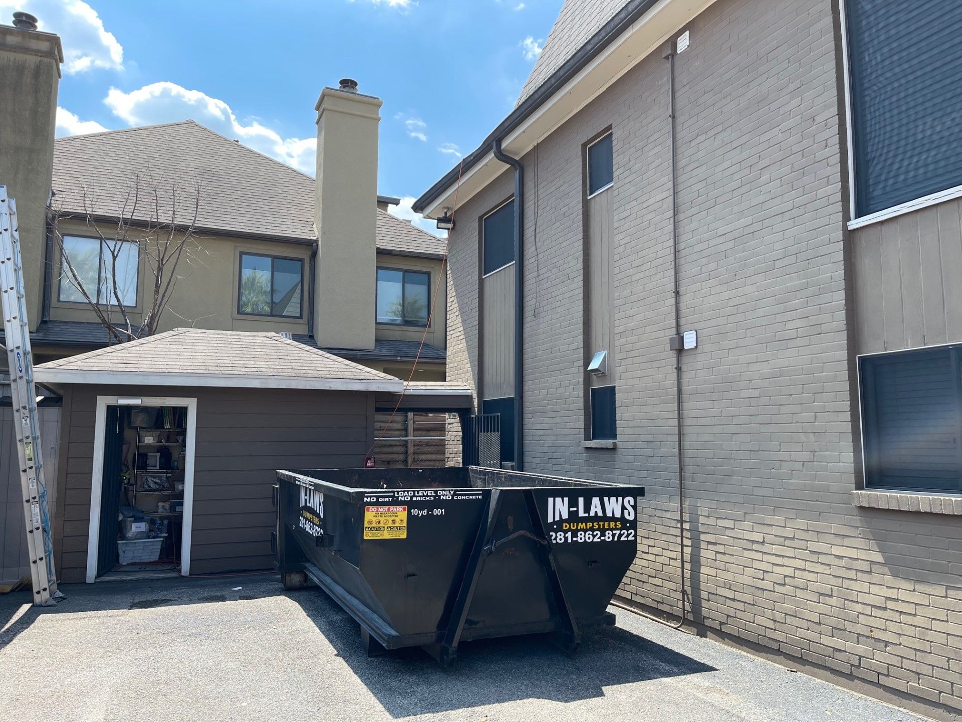 A dumpster is parked in front of a brick building.