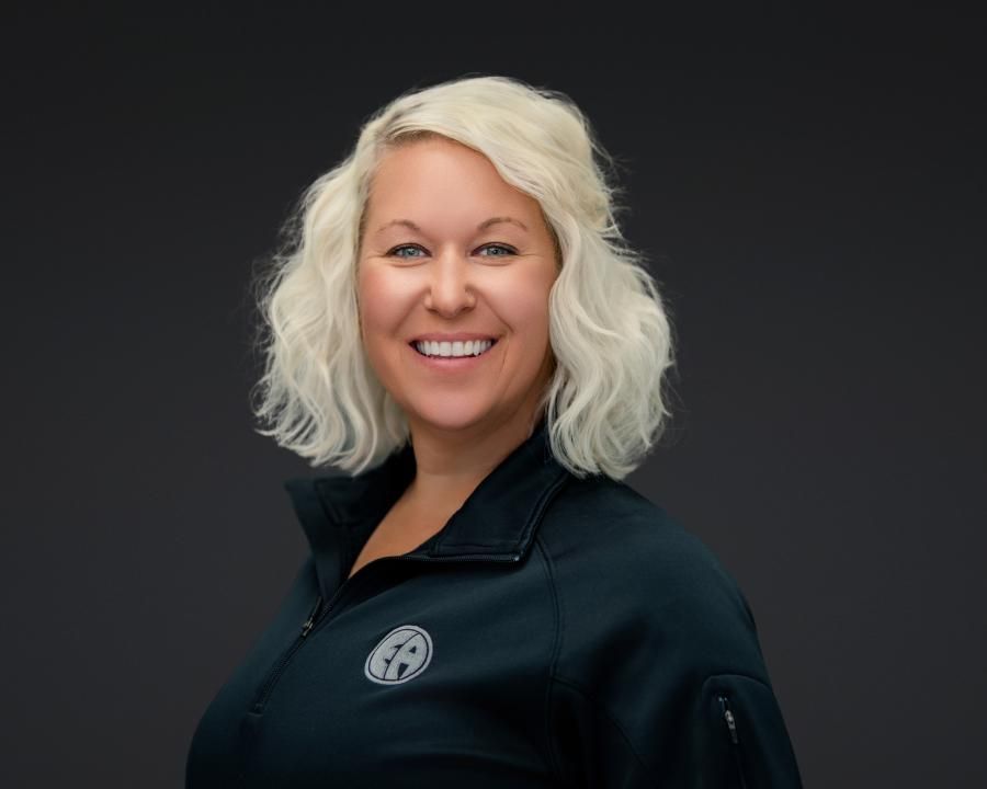 Smiling blonde person in a black jacket against a dark gray background