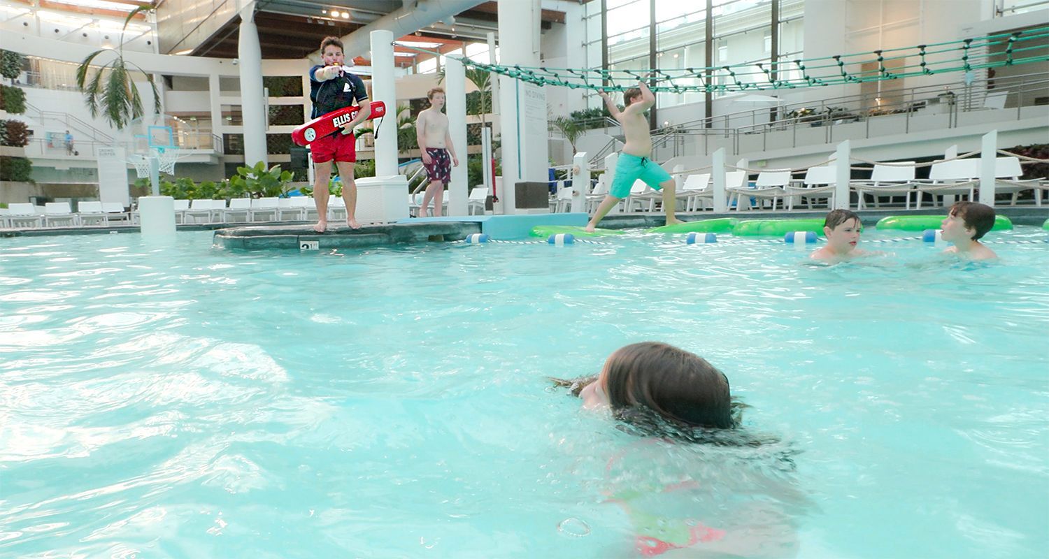 Indoor pool with swimmers, a lifeguard stand, and turquoise water splashing around the lanes