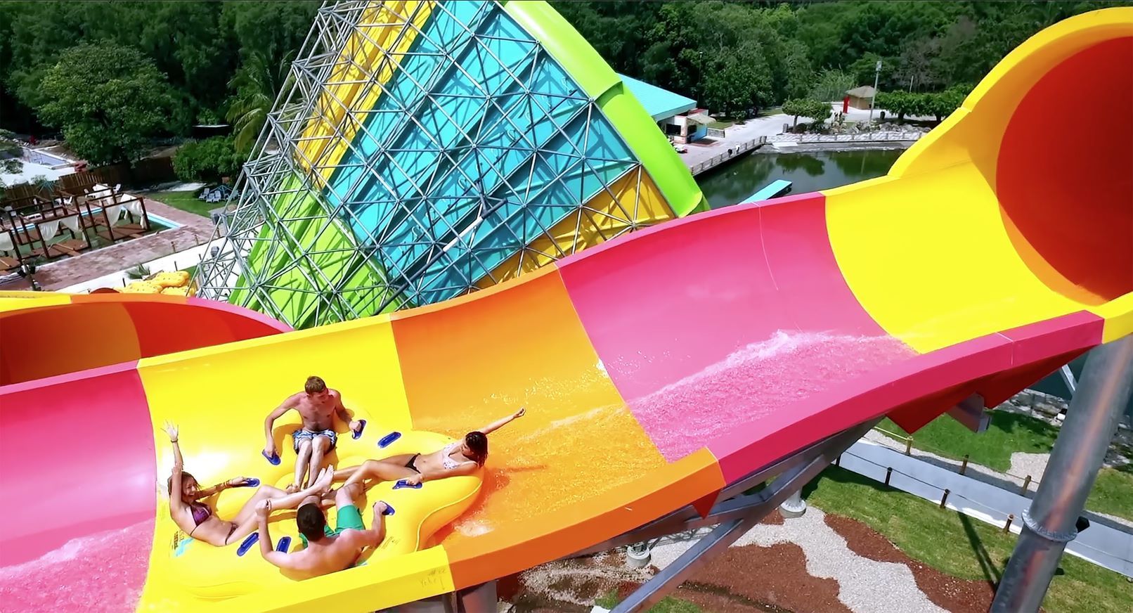 Two riders on a bright yellow, pink, and orange water slide at a theme park