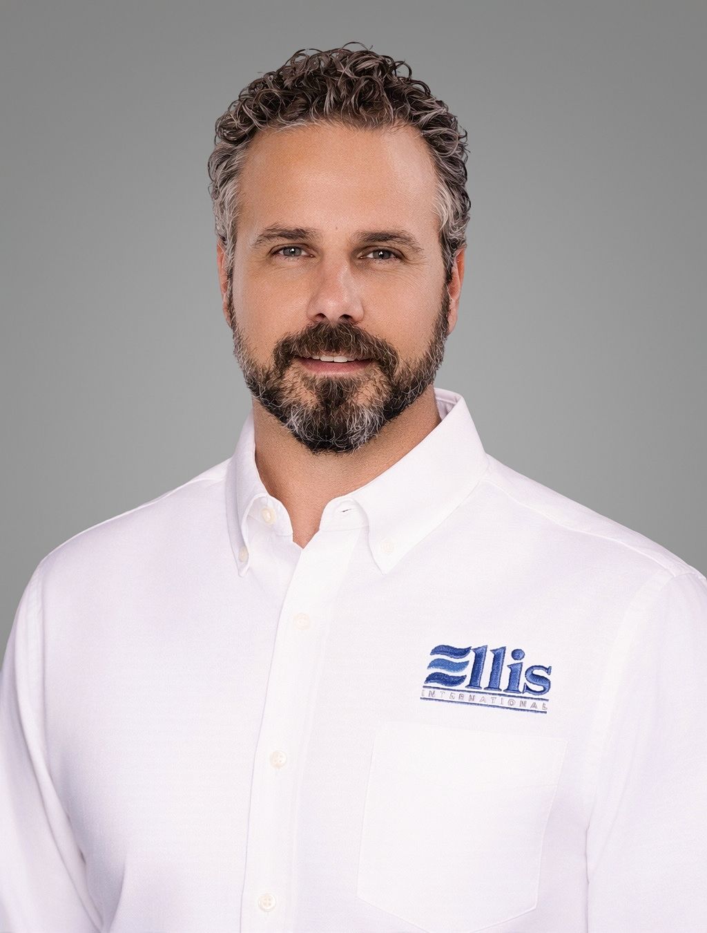 Smiling man in a white Eliis-branded shirt against a gray background