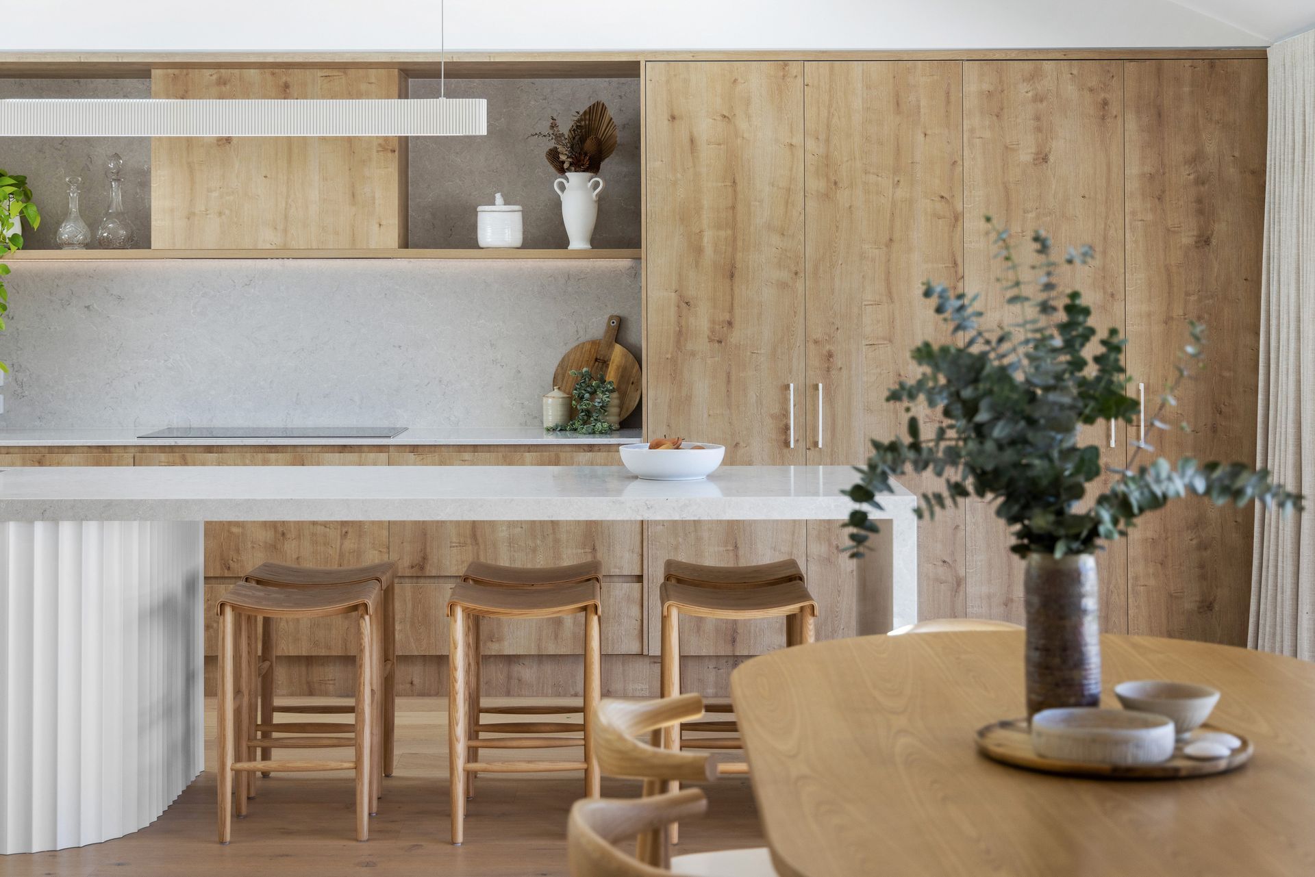 A kitchen with wooden cabinets , stools , a table and a vase of flowers.