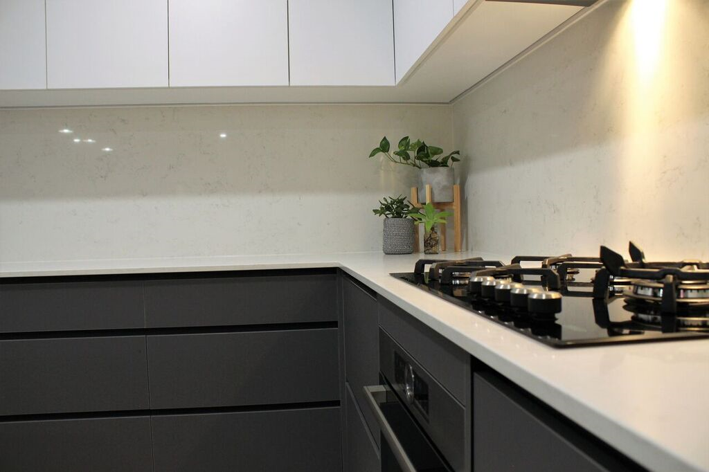 A kitchen with gray cabinets , white counter tops , and a black stove top oven.