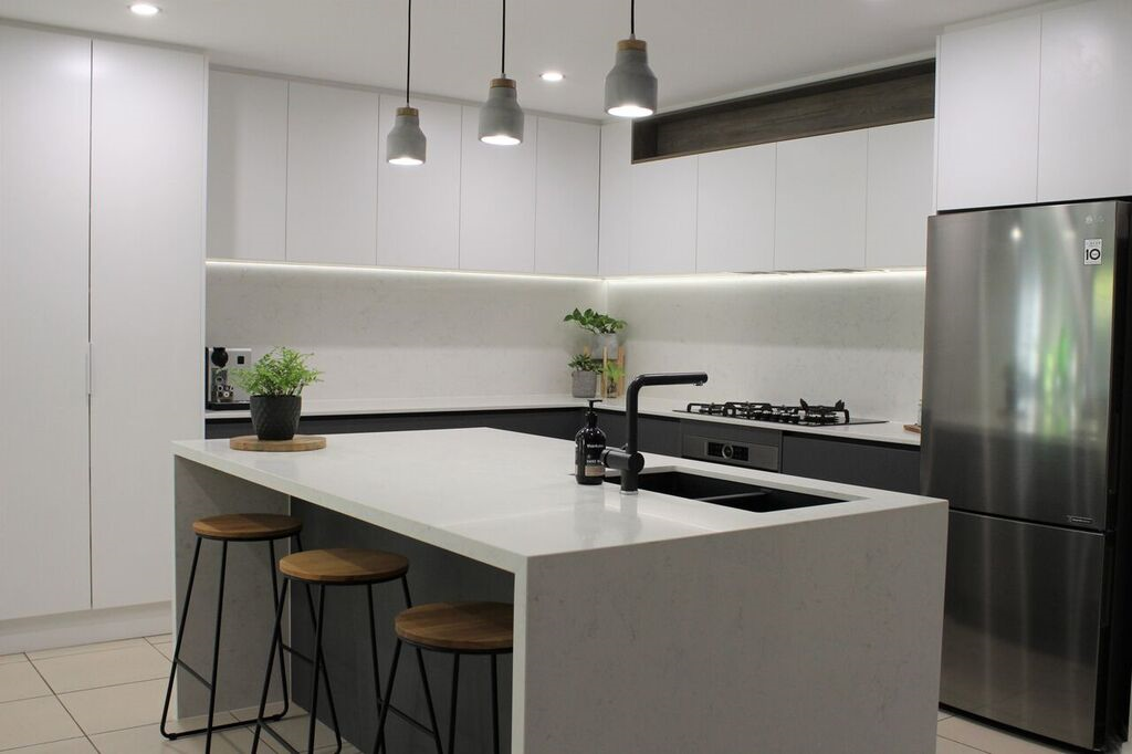 A kitchen with a large island , stools , a refrigerator and a stove.