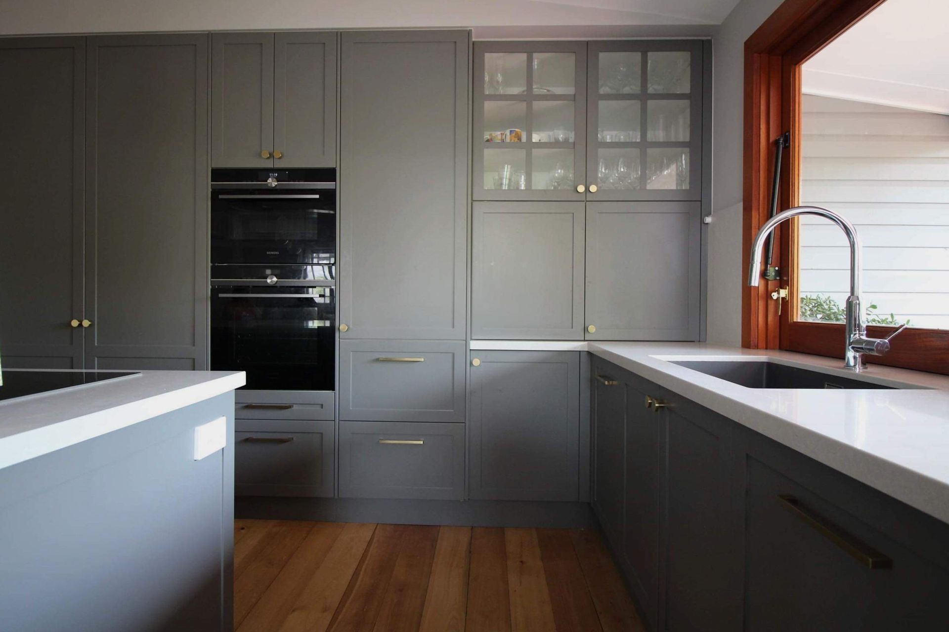 A kitchen with gray cabinets , a black oven , a sink , and a window.
