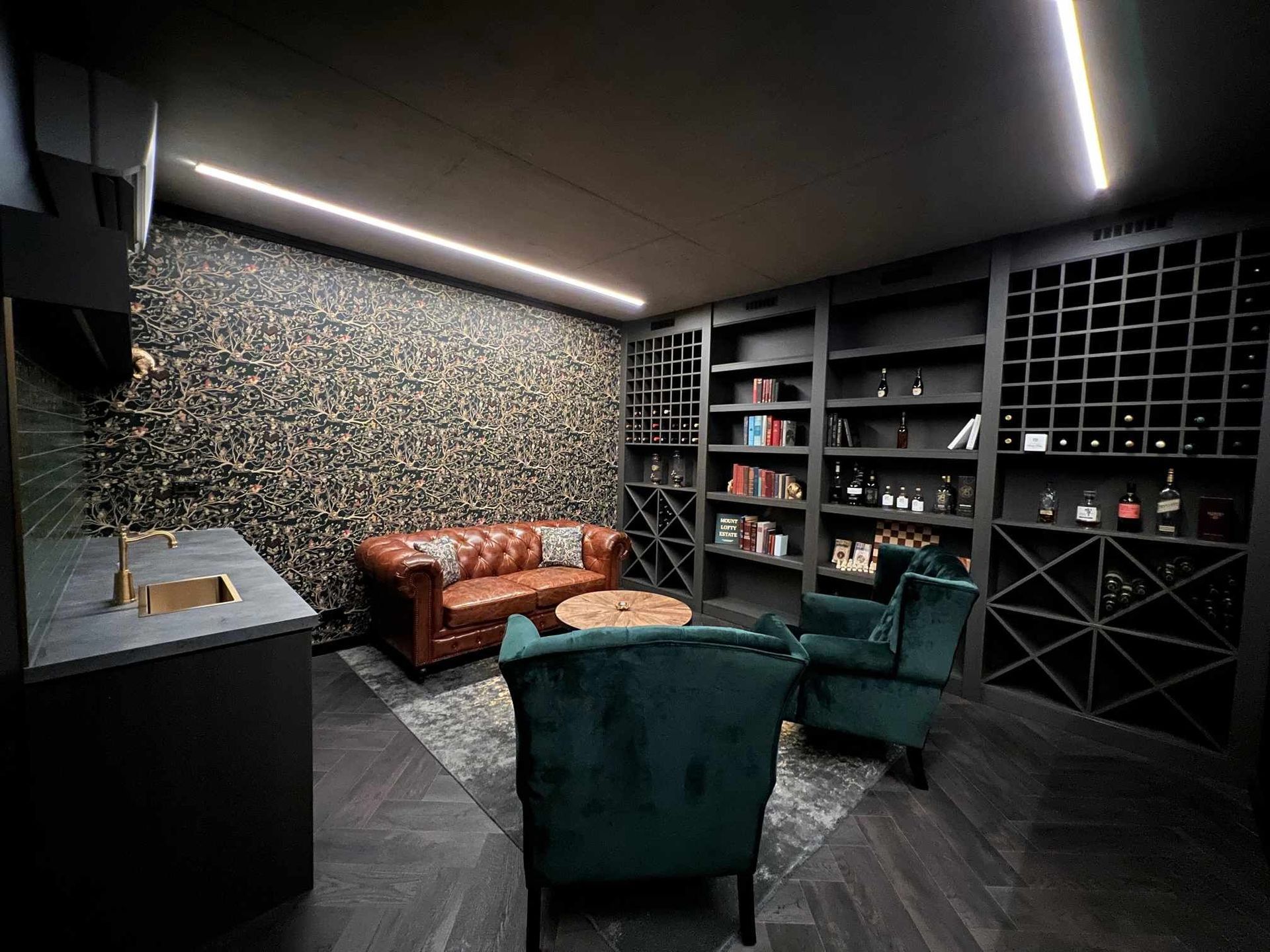 A living room with a couch , chairs , and shelves filled with wine bottles.