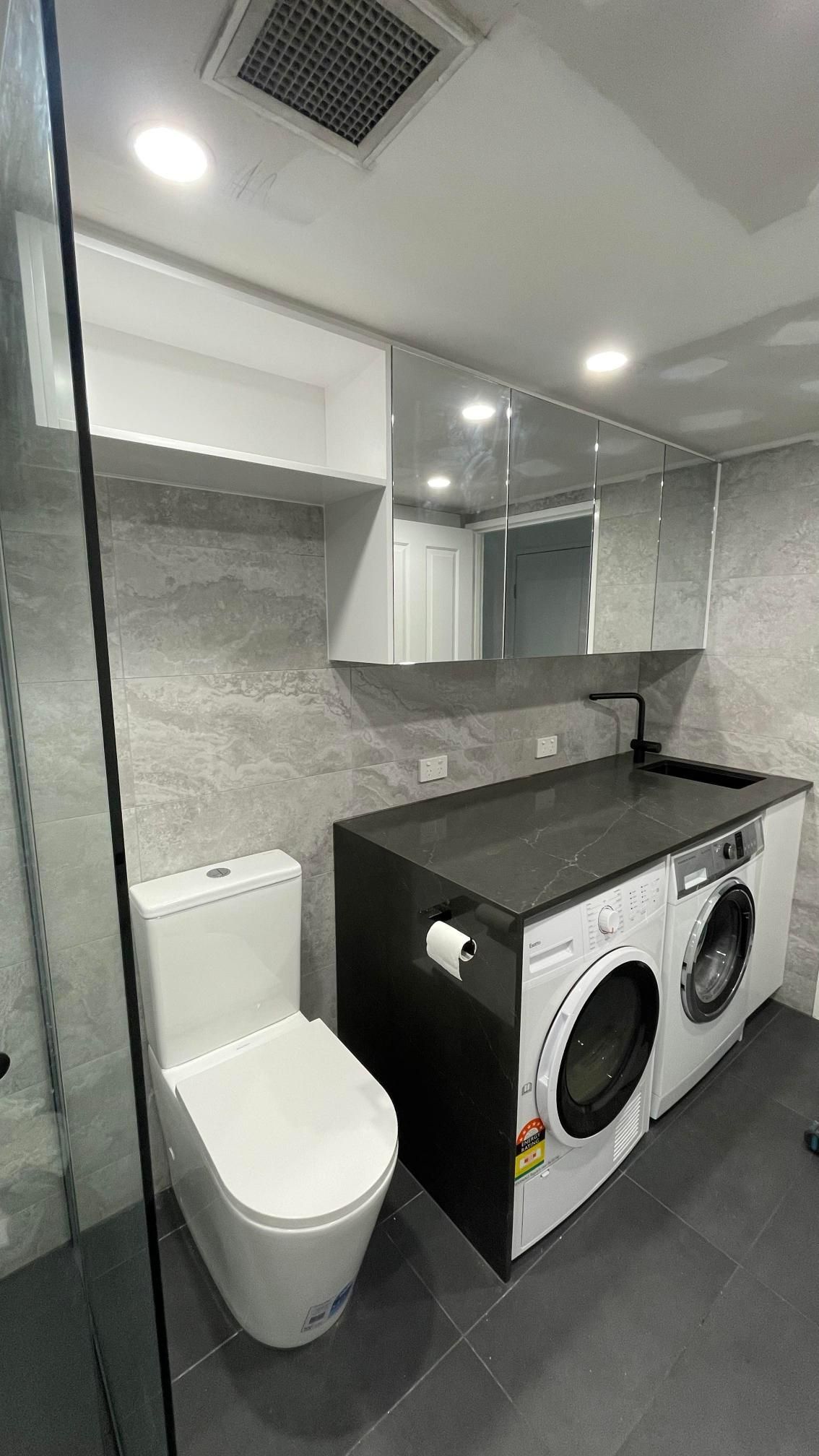 A bathroom with a toilet , washing machine , and dryer.