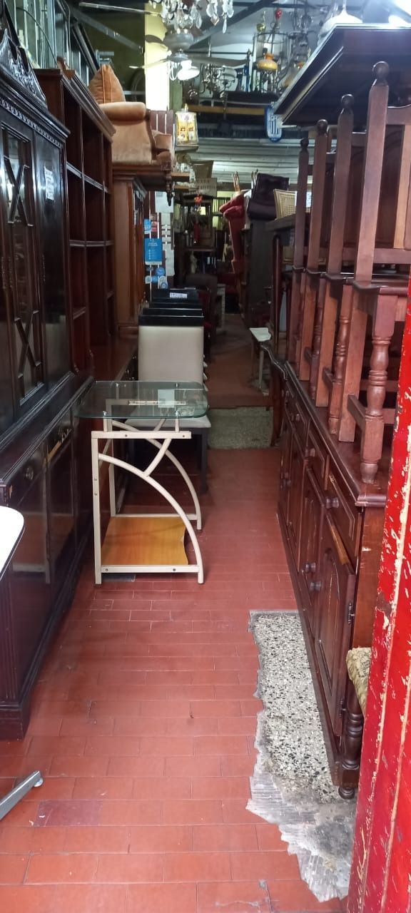 Un pasillo estrecho en una tienda repleta de muebles de madera, incluyendo armarios, mesas y una vitrina de cristal