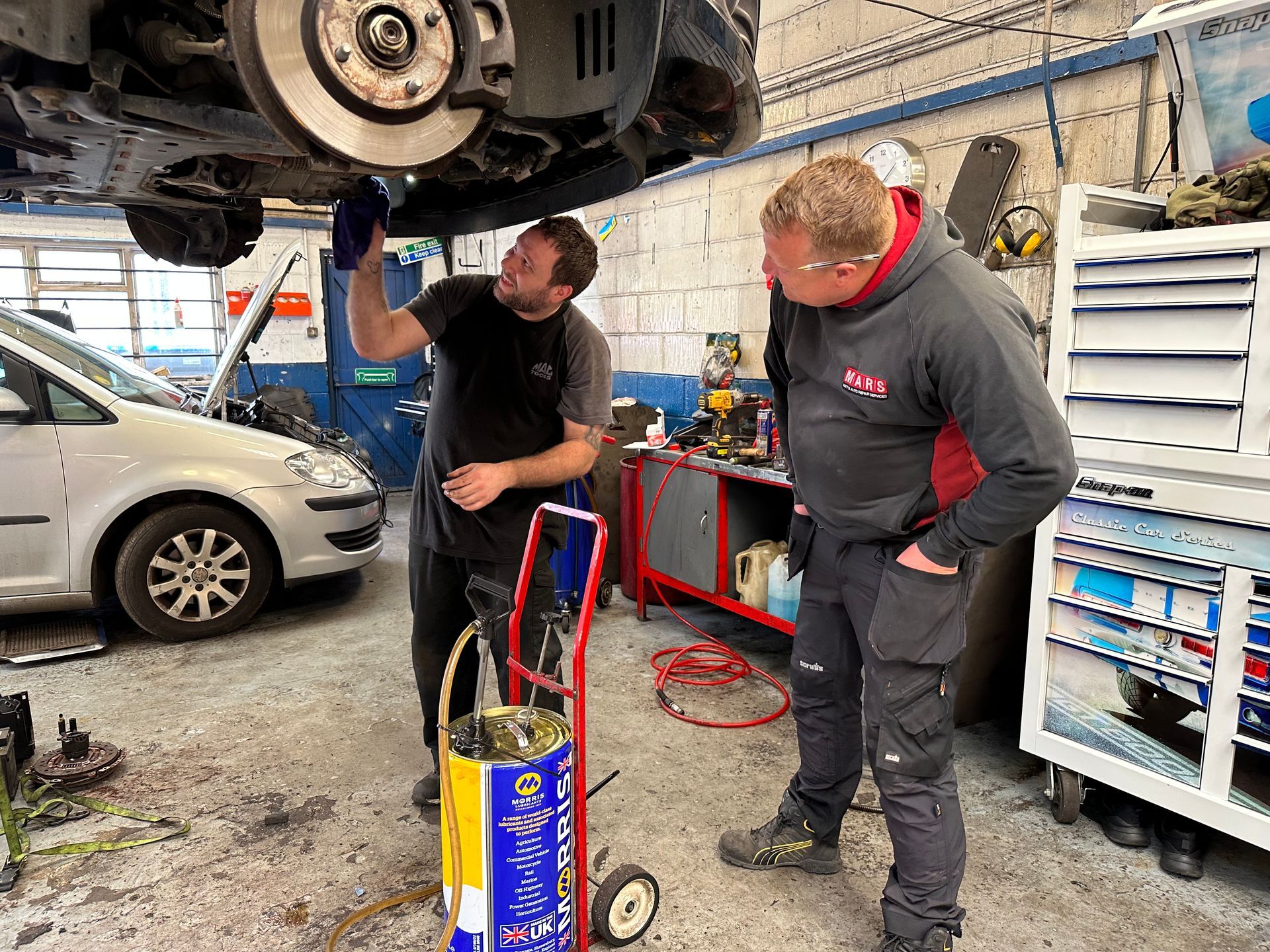 Two men are working on a car in a garage.