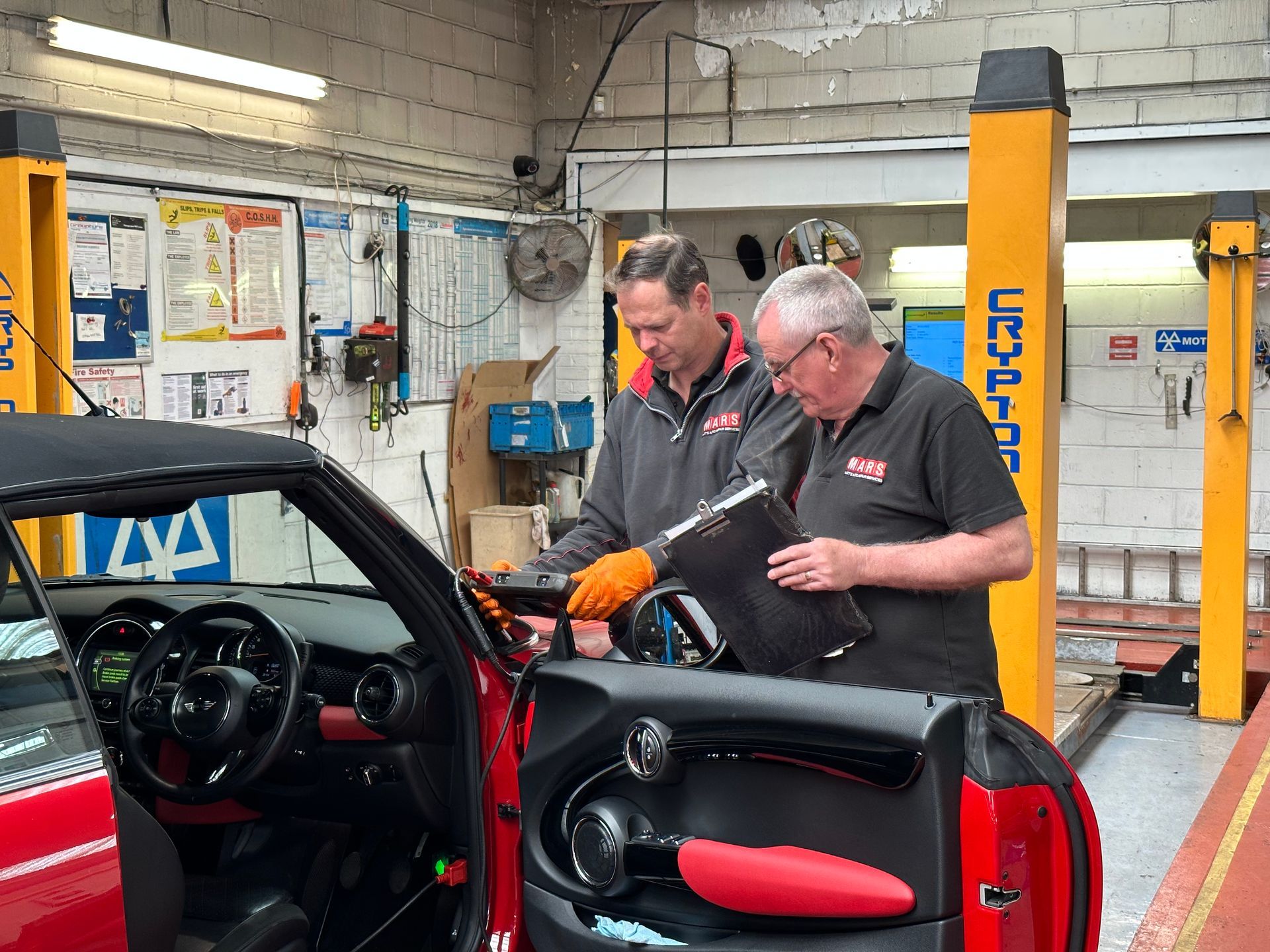 Two men are working on a red car in a garage.