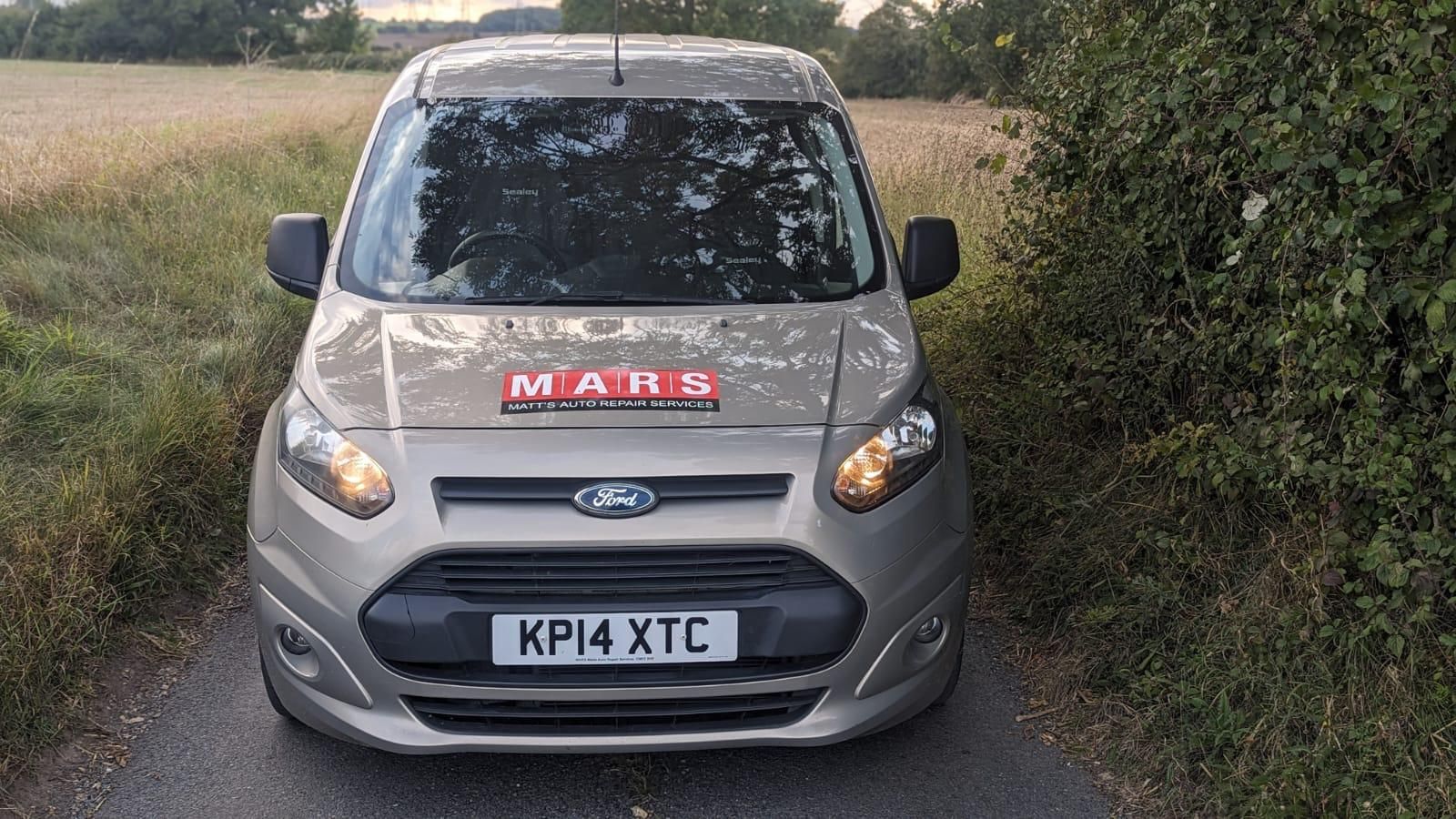A ford van is parked on the side of a road next to a field.