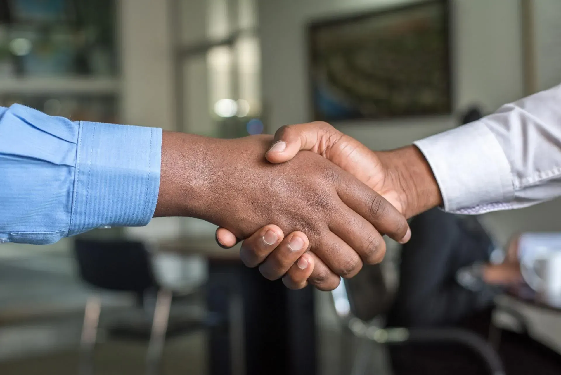 Two people shaking hands, indoors. One wearing a blue shirt, the other a white shirt.