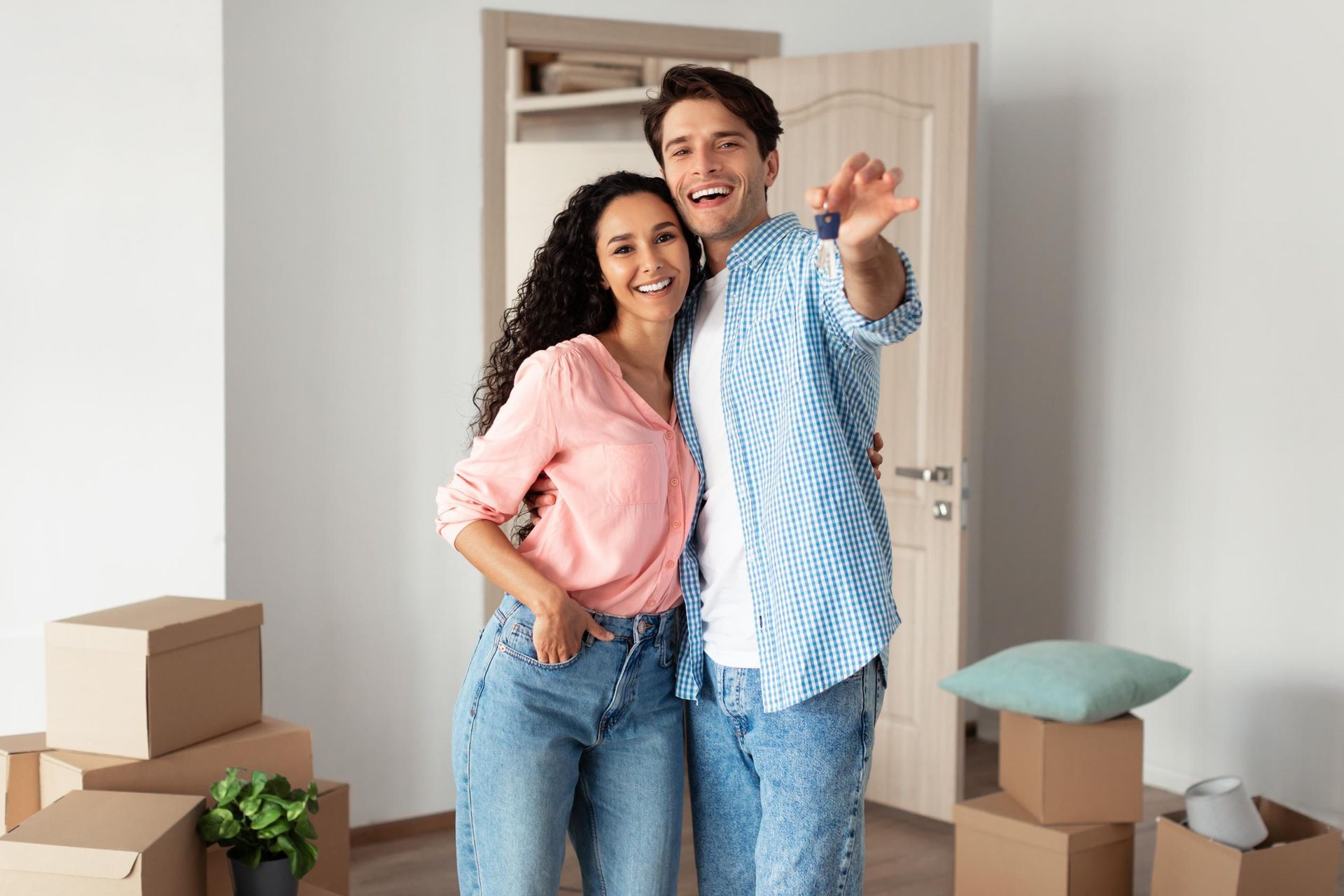 Couple in new home, holding keys, surrounded by moving boxes.