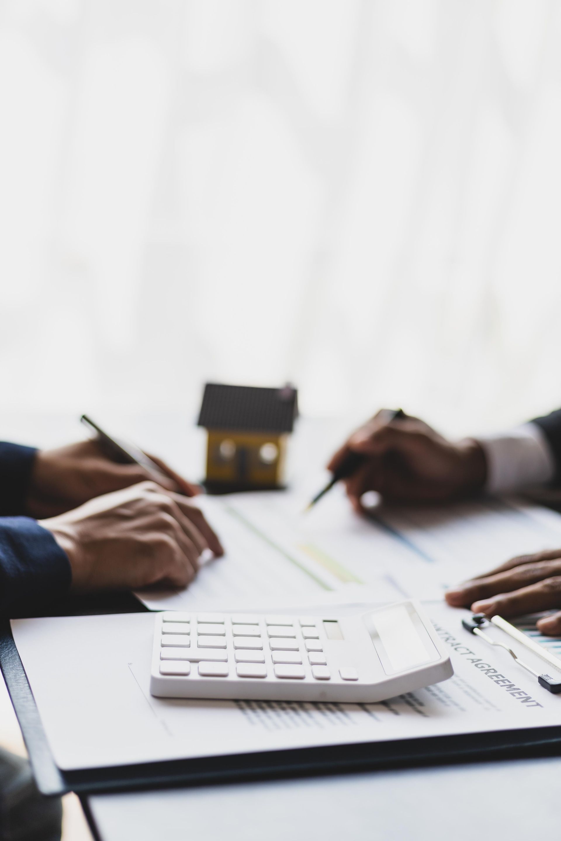 Two people reviewing documents at a table with a calculator, toy house, and pens.