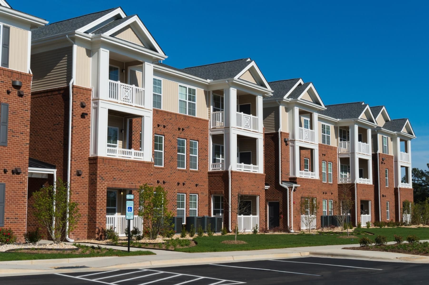 Multi-story brick apartment building with white trim, balconies, and blue sky.