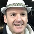 A man wearing a white hat and a black jacket is smiling.
