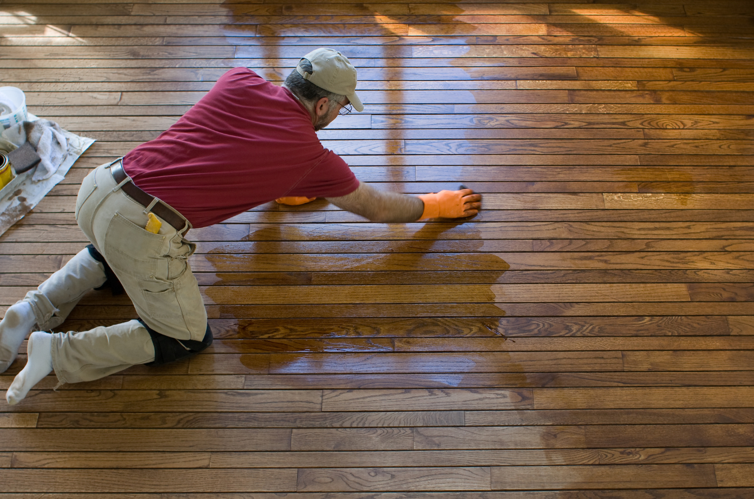 man in a red shirt polishing and refinishing the hardwood floor