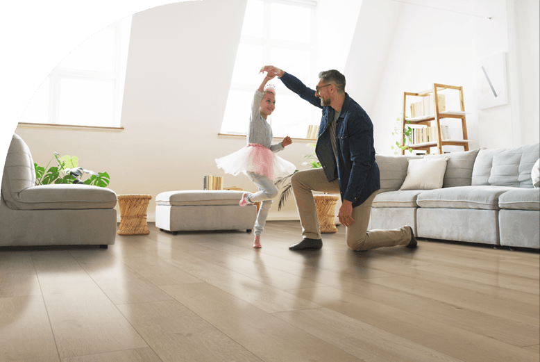 A father and daughter happily dancing around their living room with new floors