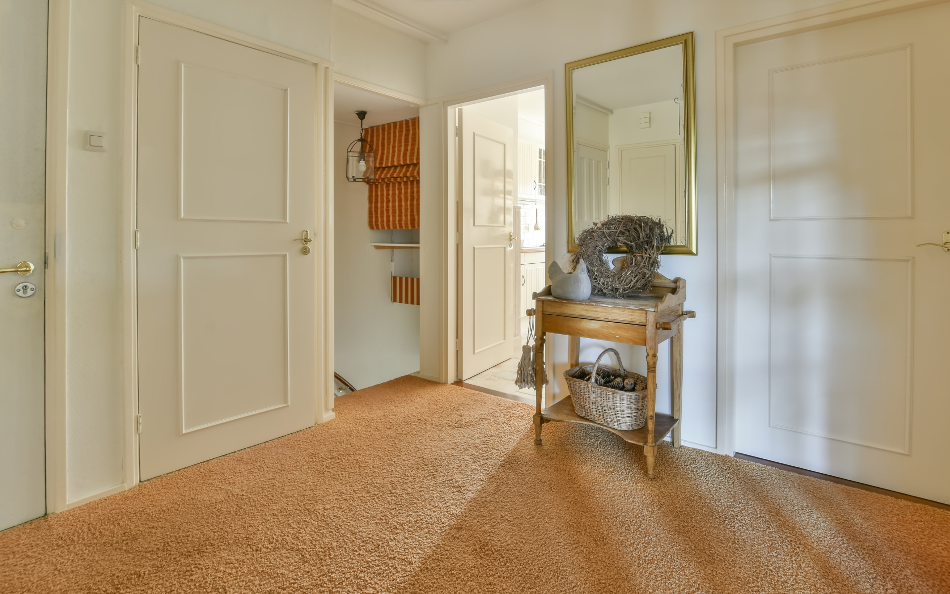 A carpeted hallway with a table and a mirror in a house.