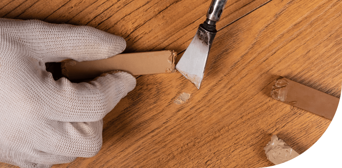 Colored putty being applied to wood floor gouges
