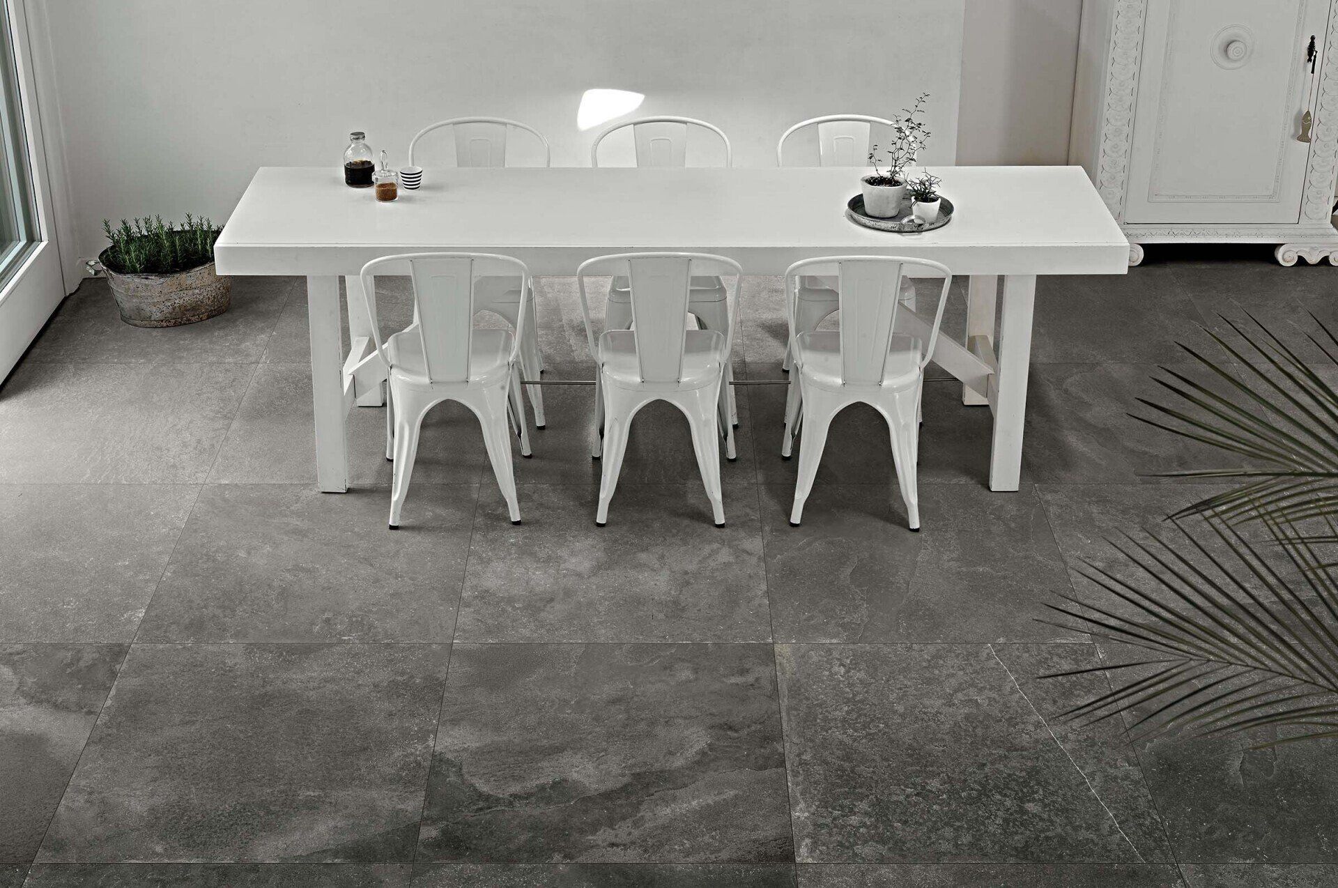 Dining room with a large white dining table and chairs on a slate grey tile floor.